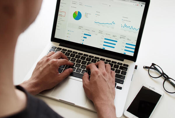 user typing at laptop with graphs visible on screen
